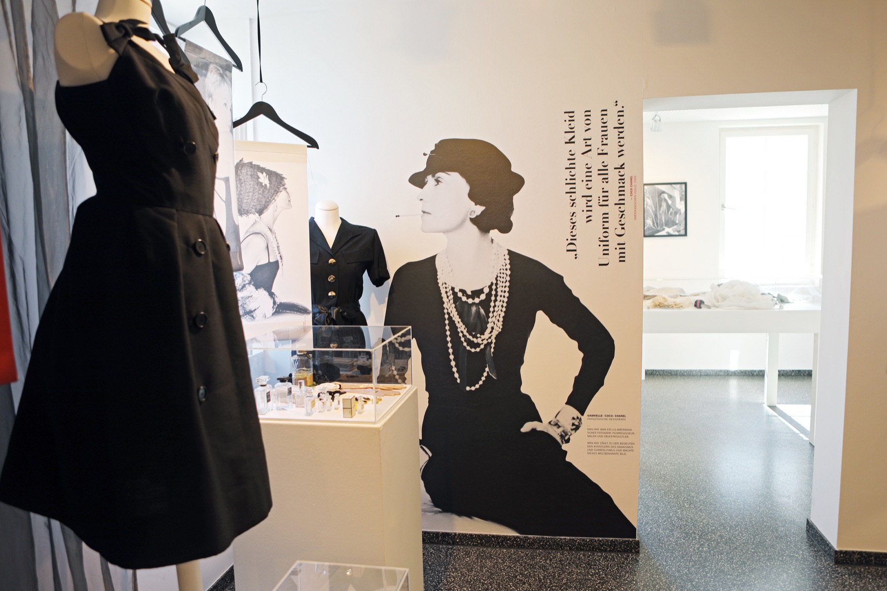 Ausstellungsansicht mit historischen schwarzen Kleidern und einer Wandgrafik von Coco Chanel