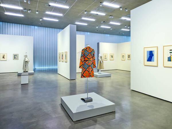 Ausstellungsansicht mit farbig gemustertem Kleid und Modezeichnungen in der Galerie Stihl Waiblingen